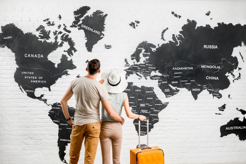 Steuerberatung für die Touristik, Paar steht mit Koffer vor der Weltkarte