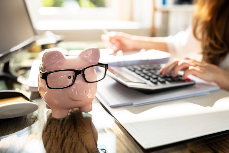Mitarbeiterin arbeitet in der Steuerkanzlei an der Finanzbuchhaltung, Sparschwein mit Brille